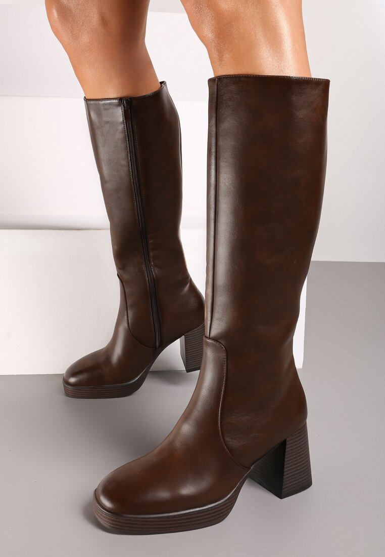 Bottes hautes en simili cuir marron avec un talon bloc et des détails en zip. Texture lisse et bout rond. Semelle robuste avec des rayures horizontales.