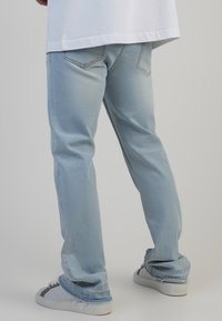 Svetlo modri denim hlače s sproščenim fitom, z ravnimi nogavicami, kontrastnim šivanjem in raztrganim robom. V kombinaciji z belimi športnimi copati.