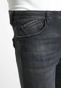 Jean en denim noir avec un design classique à cinq poches, fermeture éclair et un léger délavage. Le tissu a une texture lisse avec un léger éclat.
