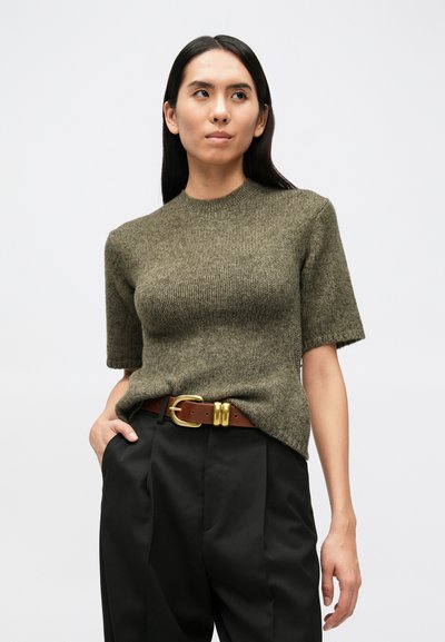 Olívovo zelený krátky rukávový sveter s okrúhlym výstrihom a vrúbkovanou textúrou, skombinovaný s čiernymi nohavicami s vysokým pásom a hnedým opaskom so zlatou prackou.