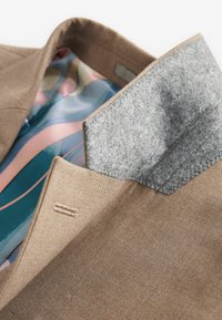 Brauner Blazer mit glatter Textur, grauem Filzkragen und buntem, gemustertem Futter in Blau-, Rosa- und Beigetönen.