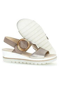 Slingback sandals with a beige and metallic silver upper, featuring a large round accent and a white textured outsole.