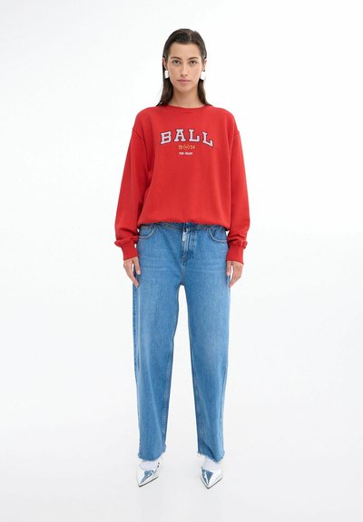 Rød sweatshirt med teksten "BALL 1924", parret med lyseblå vide bukser og hvide spidse sko. Glat stof og afslappet pasform.