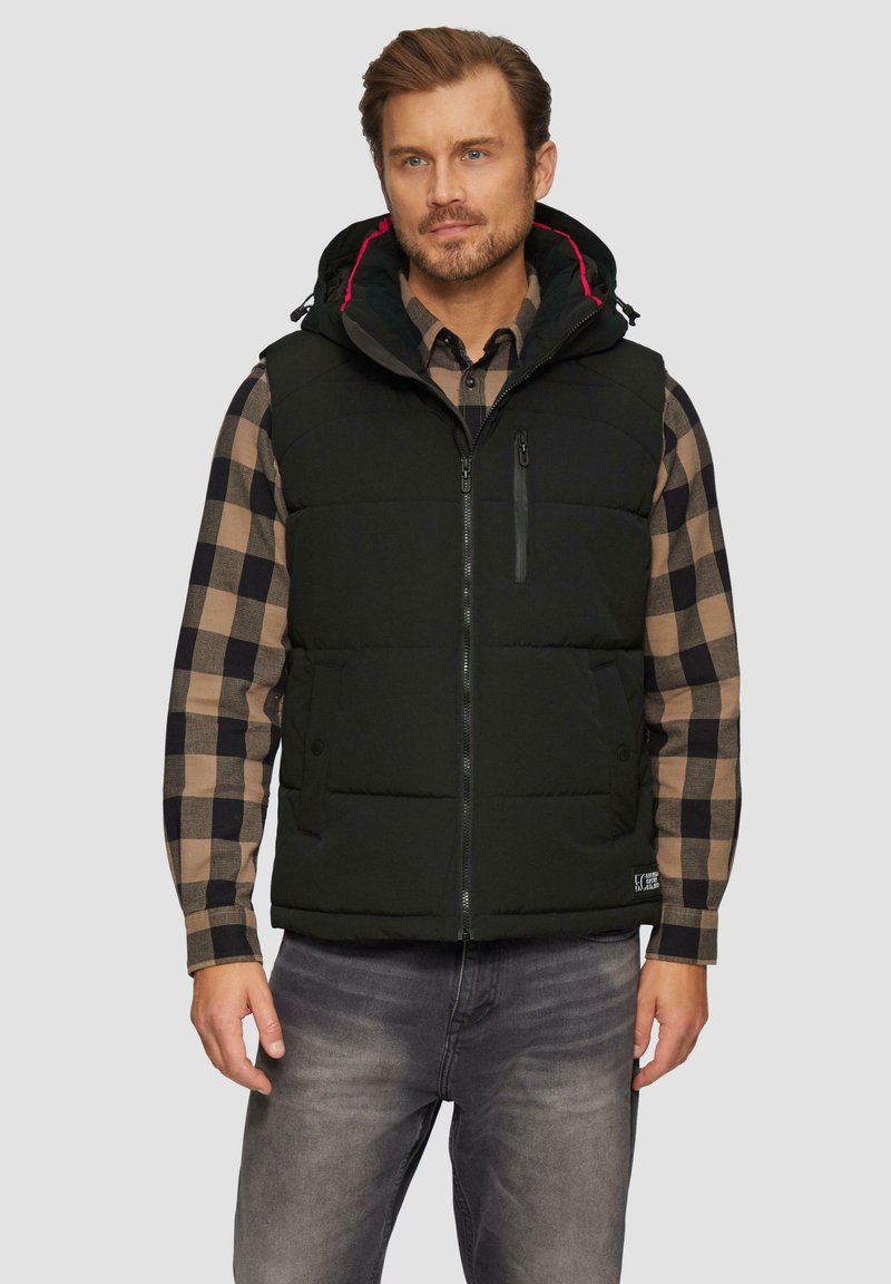 Schwarze gepolsterte Weste mit abnehmbarem Kapuze, Reißverschluss vorne und Taschen; getragen über einem braun-schwarz karierten Hemd; zeigt ein lässiges Design.