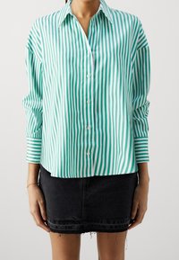 Grün-weiße gestreifte Knopfhemd mit Kragen, langen Ärmeln und einer lockeren Passform. Kombiniert mit einem schwarzen Jeans-Minirock.