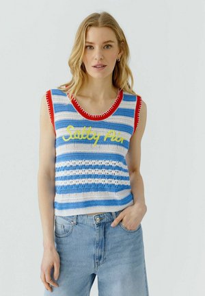 Frau mit blondem Haar trägt ein ärmelloses blau-weiß gestreiftes Strickoberteil mit rotem Besatz und gelbem "Salty Air"-Schriftzug, kombiniert mit hellblauen Jeans.
