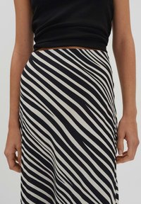 Gonna a righe bianche e nere con linee diagonali, texture liscia e vita aderente, indossata con un top nero aderente.