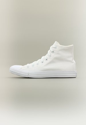 Baskets montantes en toile blanche avec semelle et embout en caoutchouc blanc, vues de côté sur un fond clair uni.