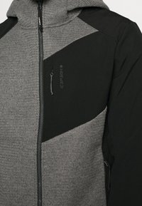 Gray and black zip-up jacket with a hood; features textured fabric, geometric color blocking, and a zippered pocket on the left chest.
