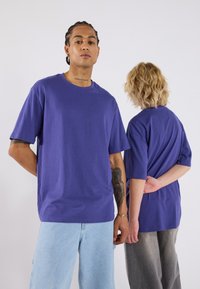 Divi cilvēki valkā brīvus, īsām piedurknēm purpura t-kreklus. Viens ir vērsts uz priekšu, bet otrs ir pagriezies prom. Ikdienišķi džinsi un pelēki apģērba apakšdaļas.