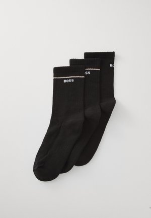 Schwarze Baumwollsocken mit gerippter Textur, ausgestattet mit dem weißen "BOSS"-Logo und einem kontrastierenden weißen Streifen oben. Drei Paare ausgestellt.