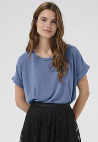 Mėlynas trumpomis rankovėmis marškinėliai su apvaliu iškirpimu, pagaminti iš lygaus audinio. Sujungti su juodu nėriniuotu sijonu, turinčiu prigludusį juosmenį.