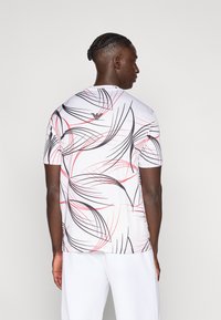 Λευκό κοντομάνικο t-shirt με στροβιλιστές μαύρες και κόκκινες γραμμές, διαθέτει στρογγυλή λαιμόκοψη και απαλό, ελαφρύ ύφασμα.