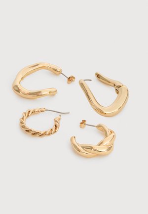 Τέσσερα ζευγάρια σκουλαρίκια κρίκοι σε χρυσό τόνο με διαφορετικά σχέδια: στριφτά, λεία και χοντρά, καθώς και μεγάλοι ανοιχτοί κρίκοι σε λευκό φόντο.