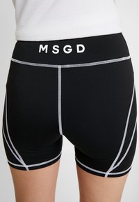 Czarne spodenki sportowe z białym przeszyciem i logo "MSGD" na pasku. Charakteryzują się dopasowanym krojem i krótką długością dla wygody.