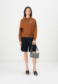 Brown zip-up sweatshirt, navy shorts, black open-toe heels, and patterned handbag with a shoulder strap. Simple, casual outfit elements.