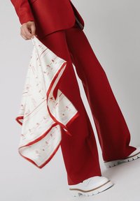 Czerwony dopasowany garnitur z szerokimi spodniami, w zestawie z białym jedwabnym szalem w czerwone wzory. Całość dopełniają białe buty na platformie.