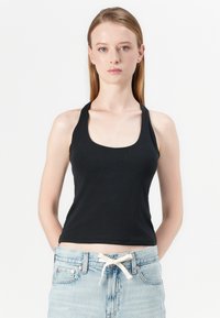 Black fitted tank top with a scoop neckline and racerback design, made from smooth fabric, paired with light blue high-waisted jeans.