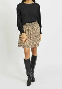 Svart långärmad topp i kombination med en beige mönstrad kjol och knähöga svarta läderstövlar, som visar en avslappnad passform och texturerad design.