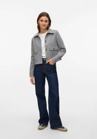 Grau gekürzter Blazer mit Knopfverschluss, zwei Brusttaschen und Kragen, kombiniert mit dunkelblauen Schlagjeans und legerem Schuhwerk.