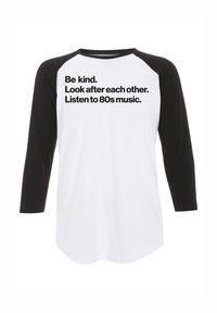 Baseballstijl shirt met een witte body en zwarte raglanmouwen. Voorzien van vetgedrukte zwarte tekst: “Wees vriendelijk. Zorg voor elkaar. Luister naar 80s muziek.”
