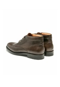 Une paire de bottes en cuir marron foncé montantes avec des lacets, des semelles noires et une doublure intérieure beige, vue d'un angle arrière.