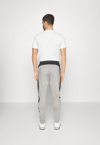 Grå idrottsbyxor med svarta sidodetaljer, elastisk midja och smalnande ben, kombinerade med en enfärgad vit T-shirt och vita sneakers.