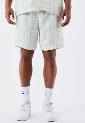 Pantaloni corti a scacchi verde chiaro in un tessuto testurizzato, con orlo grezzo. Abbinati a calze sportive bianche e sneakers.