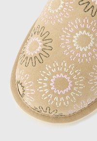 Μύτη παπουτσιού από μπεζ ύφασμα με κεντητά λουλουδένια σχέδια σε ροζ, λευκό και μαύρο νήμα, με περίτεχνη υφασμάτινη μπορντούρα στην άκρη.