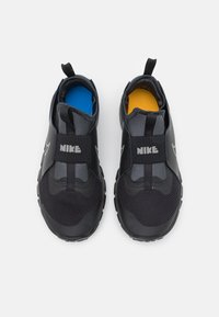 Czarne slip-ony Nike z teksturowaną cholewką, z solidnym czarnym paskiem oraz kontrastowymi niebieskimi i żółtymi wkładkami. Gumowa podeszwa zapewniająca przyczepność.