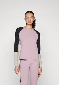 Langermet sportstop i lys rosa med svarte raglanermer. Stoffet er mykt; har kontrasterende sømmer og en liten logoakcent.