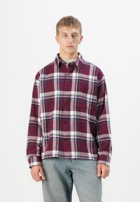 Rutig flannel-shirt i bordeaux, hvid og blå nuancer. Har knaplukning fortil, lange ærmer og en brystlomme. Blød tekstur.