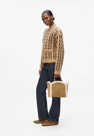 Tan knitted sweater with black pattern, front pocket, and gold buttons. Dark denim jeans, leopard print flats, and a cream-lined handbag.