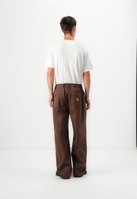 Braune weite Hosen mit einem elastischen Bund und zwei hinteren Taschen. Kombiniert mit einem schlichten weißen Kurzarmhemd. Minimalistisches Design.