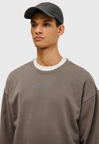 Grå sweatshirt med blå "HALO"-logotyp på bröstet, med rund halsringning och avslappnad passform. Matchande grå keps med perforerade paneler.