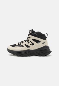 Beige und schwarze Wanderschuhe im High-Top-Design verfügen über ein strukturiertes Obermaterial aus Stoff, eine robuste schwarze Gummisohle und ein Schnürdesign mit seitlichen Ausschnitten.