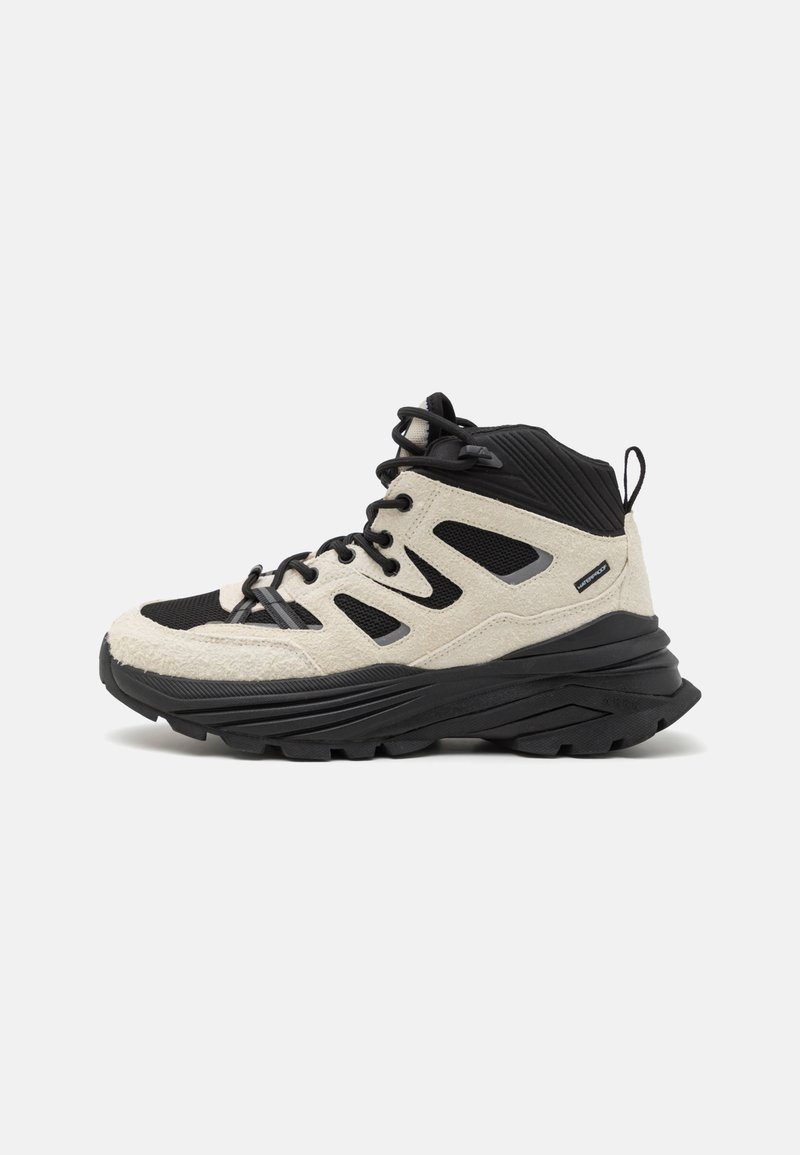 High-top hiking shoes in beige and black features a textured fabric upper, sturdy black rubber sole, and lace-up design with side cutouts.