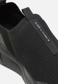 Sneaker nera con tomaia in mesh testurizzato e linguetta, decorata con coordinate di latitudine e longitudine bianche sul lato.