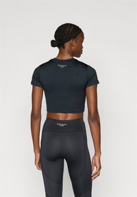 Sort kort aktiv t-shirt med korte ærmer, glat tekstur og logo detaljer bagpå. Kombination med sorte højttaljede leggings med sømdetaljer.