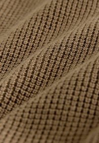 Textúrovaná hnedá tkanina s tkaným vzorom, obsahujúca vystúpené a prehĺbené prvky vytvárajúce štruktúrovaný vzhľad. Mäkký a mierne chlpatý povrch.