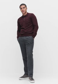 Burgundy neulepaita, jossa on kolme nappia, yhdistettyinä hiilenharmaisiin housuihin. Harmaat lenkkarit valkoisilla pohjilla täydentävät asua.