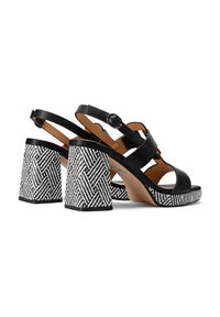 Sandali neri in pelle con un tacco spesso a blocco bianco e nero stampato. Presentano una cinghia regolabile alla caviglia e un design open toe.