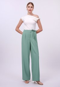 White off-the-shoulder top paired with high-waisted, light green, wide-leg trousers featuring a tied waist detail. Smooth fabric texture.