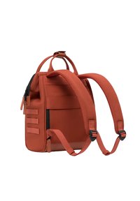 Red fabric backpack with adjustable straps, top handle, textured surface, side zip pocket, and horizontal strap accents on one side.