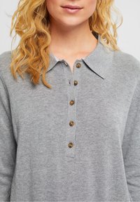 Polo shirt grigio a maglia con colletto, cinque bottoni marroni lungo la parte anteriore e tessuto strutturato, che mostra un design dalla vestibilità rilassata.