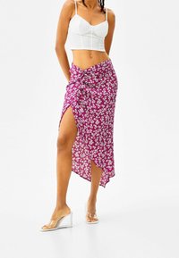 Lila blommig omslagskjol med en sidoklyfta, gjord av lättviktig tyg, med en knutdetalj vid midjan. Matchas med klara kilklackar.