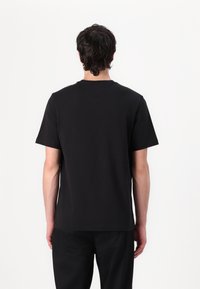 T-shirt noir à manches courtes en coton, avec un col ras du cou et un design simple et épuré. Texture lisse avec une coupe décontractée.