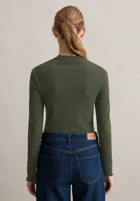Langstukken, geribbelde groene top met een gegolfde halslijn, gecombineerd met donkerblauwe denim jeans met een leren label en achterzakken.