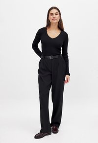 Black ribbed knit top with a V-neck, high-waisted pleated black trousers, and dark patterned slip-on shoes. Simple, fitted design.