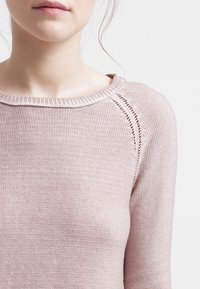 Maglione lavorato a maglia di un delicato rosa chiaro con un ampio scollo, bordi a coste e una sottile lavorazione a texture lungo le maniche. Materiale morbido e traspirante.